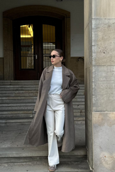 a lady in a white top, a long brown wool coat and a pair of beige pants